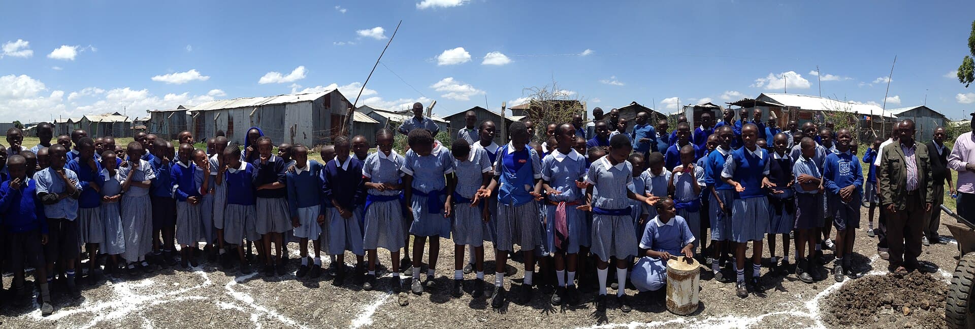 A large group of pupils in blue uniforms gathered outside their school